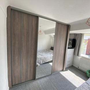 Bedroom with sliding door wardrobes, mirror, bed, and window creating space.