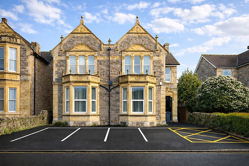 Symmetrical stone building with bay windows and paved parking area.
