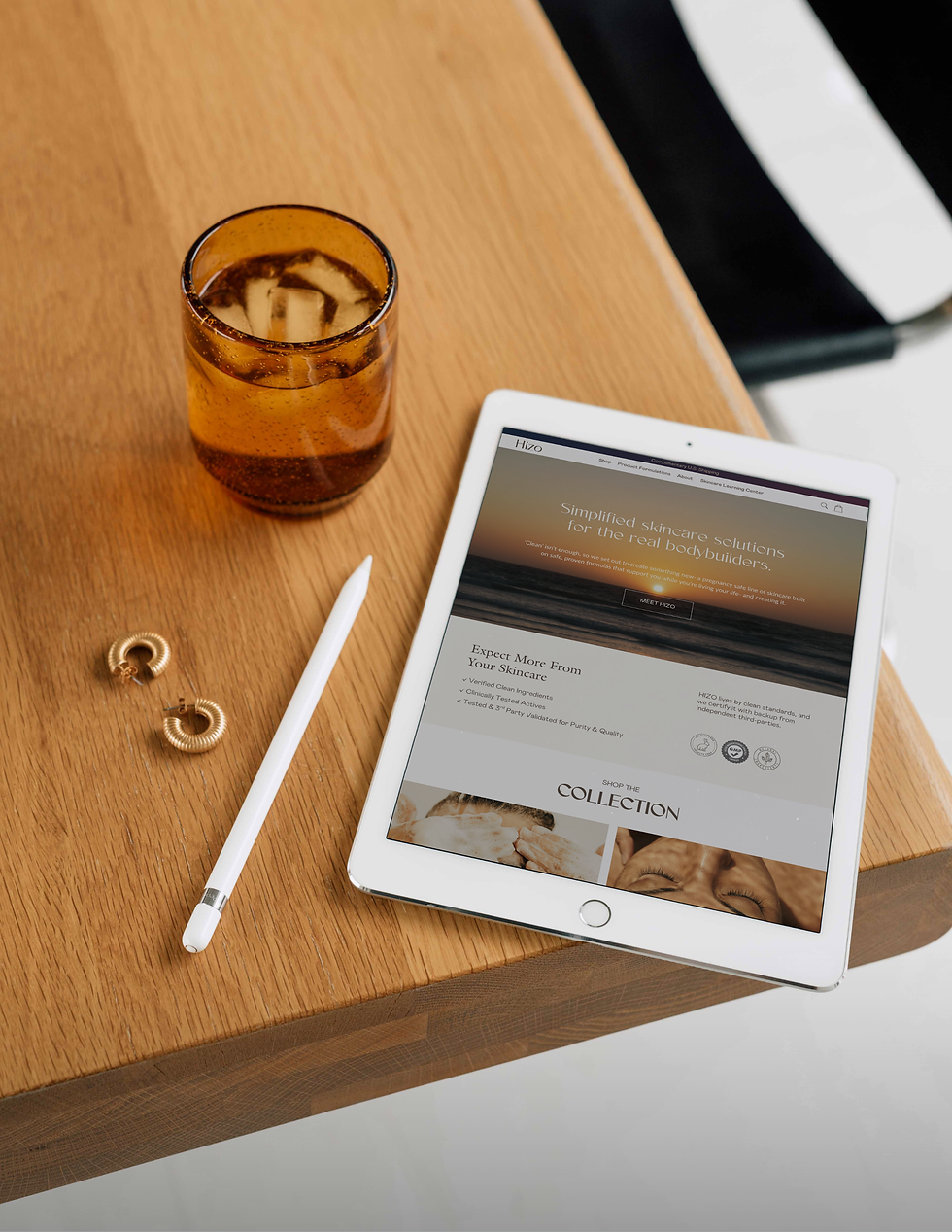 iPad laying on table next to clear glass and gold earrings, and showing clean skincare brand page