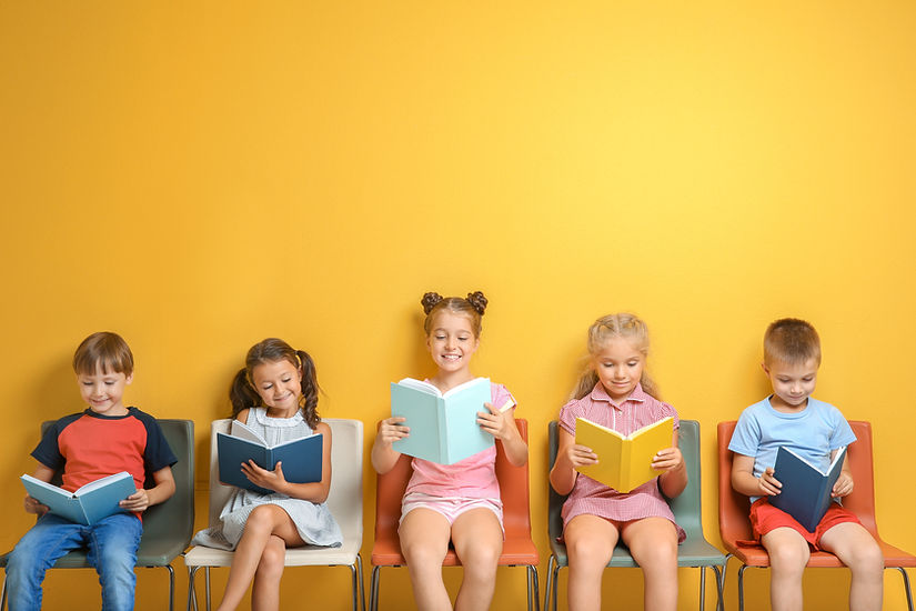 Cute little children reading books while sitting near color wall.jpg