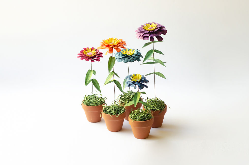 Five paper zinnia book page flowers in mini terra cotta pots, colors include hot pink, bright orange, teal, blue and purple.