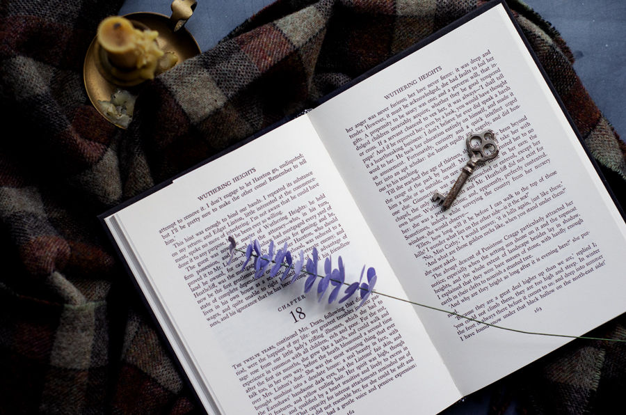 Open Wuthering Heights book with heather sprig and a skeleton key with plaid wool and a beeswax candle as a backdrop, inspired by The Moors for a moody autumn wedding theme