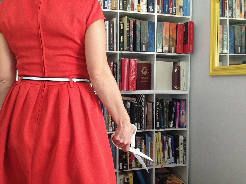 Woman in a red dress holds scissors beside a bookshelf of books, ready to start cutting.