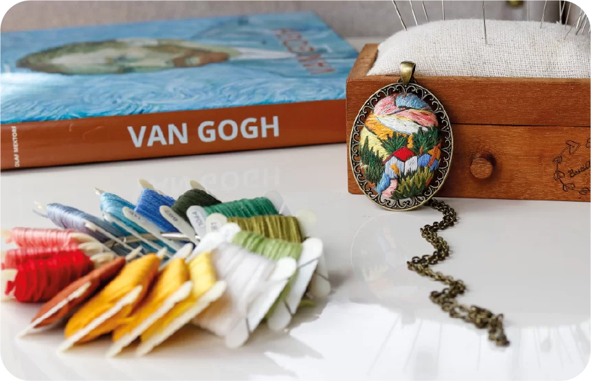 Van Gogh book next to embroidery threads and a pendant on white surface.