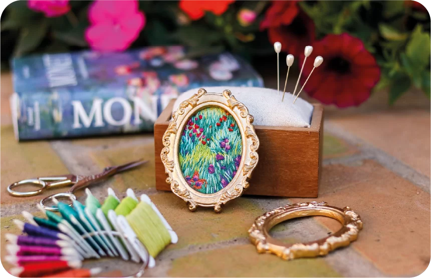 Artesanato floral e materiais de costura com livro Monet e moldura dourada.