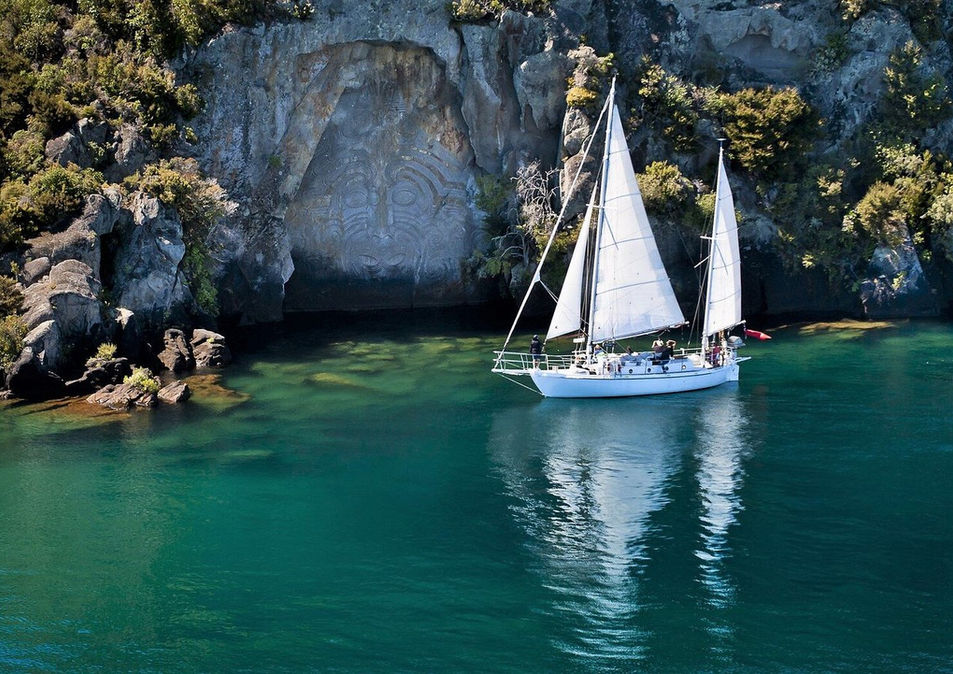 Sail Barbary positioned in front of the Māori Rock Carvings with calm turquoise water