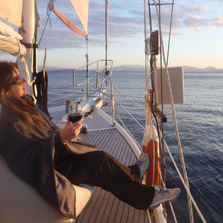 Woman enjoying a glass of wine at sunset while wrapped in a blanket on the front of a yacht.