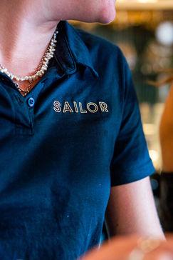 Close up of employee wearing a navy blue shirt that says SAILOR
