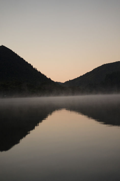 Mist over lake reflecting mountains at dawn, natural scenic background