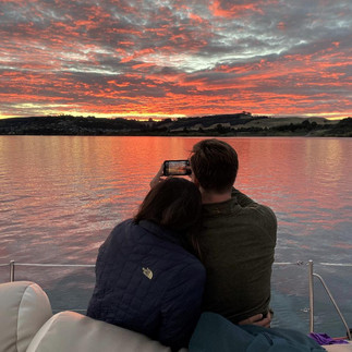 Couple snuggled on the deck of a yacht watching a vibrant red and orange sunset over Lake Taupō.
