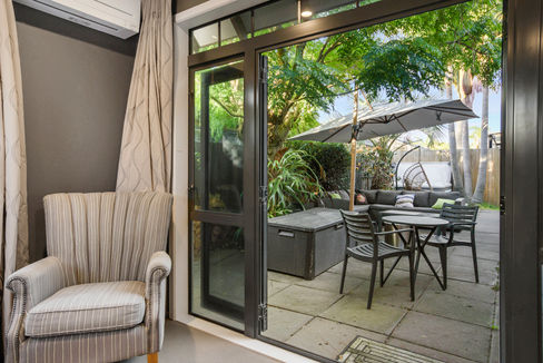Open door with outdoor patio, furniture, and lush greenery visible.