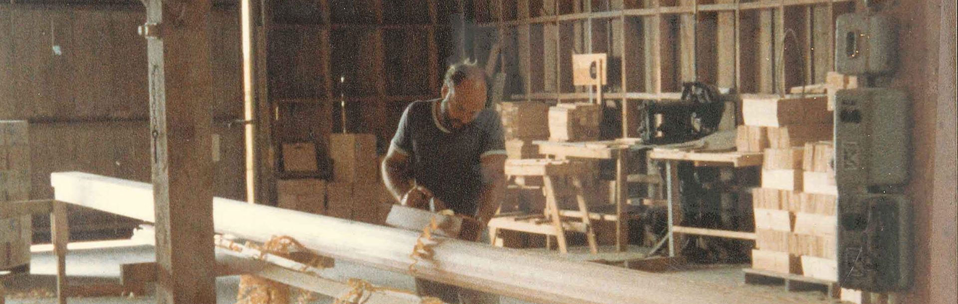 Man hand-planes long wooden plank in workshop