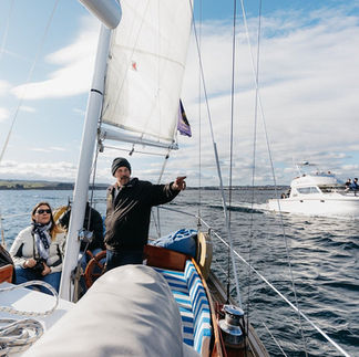 Skipper and passengers sailing aboard the Barbary yacht, pointing out views across the lake.