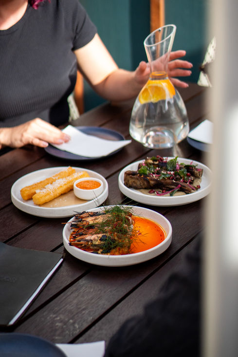 Plated dishes of food on a table, with drinks in the background IN HAUS
