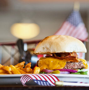 A cheeseburger with bacon and fries on a plate with an American flag