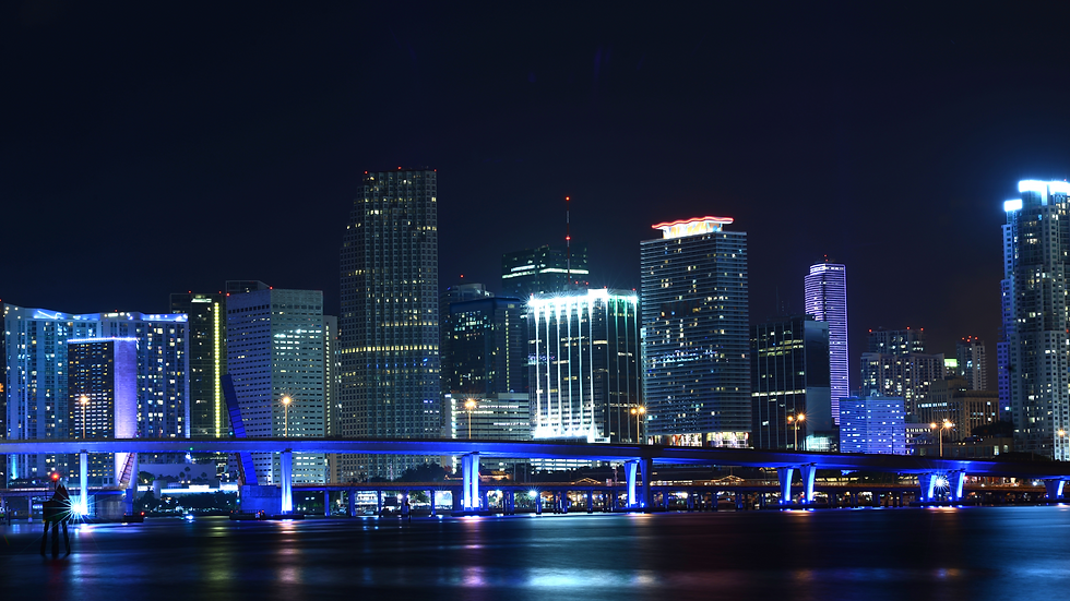 Miami skyline at night with colorful buildings and a bridge.