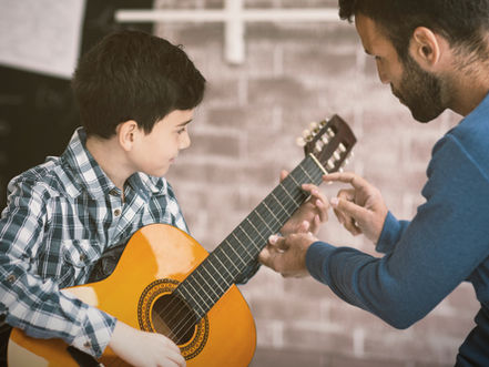 Music teacher guiding a child during a guitar lesson, illustrating the early stages of learning music and developing confidence.