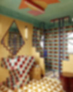 Colorful bathroom with geometric tiles in red, blue, and beige. Patterned walls, intricate ceiling design, and modern fixtures create a vibrant mood.
