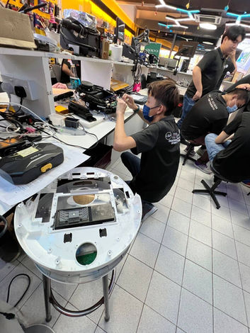 LSP technician repairing a robot vacuum cleaner in a busy workshop, surrounded by tools and electronic components.