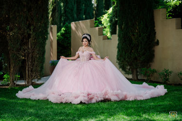 Quinceañera in a pink dress sitting on the grass with her gown spread out around her.
