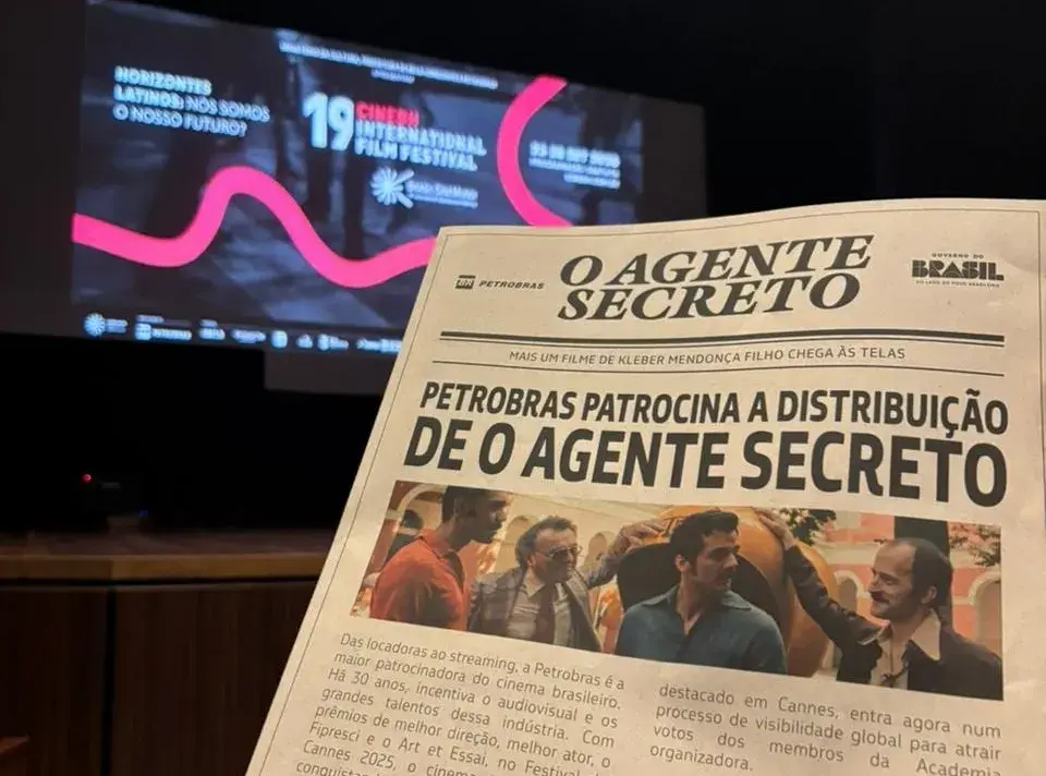Jornalzinho de O Agente Secreto distribuído durante exibição do longa na 19º CineBH em primeiro plano, diante de tela onde se lê "19º CineBH"
