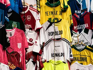 Várias camisas de times de futebol diferentes. É possível ler nomes de vários jogadores como "Ronaldo" e "Neymar"