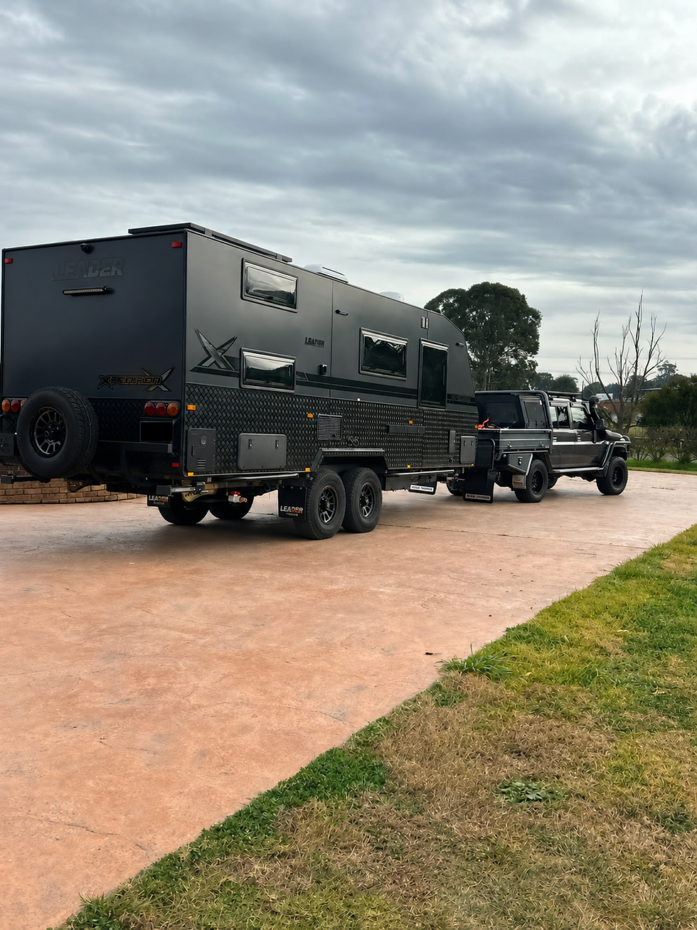Landscape photo of a dark caravan and 4WD on a driveway under cloudy sky