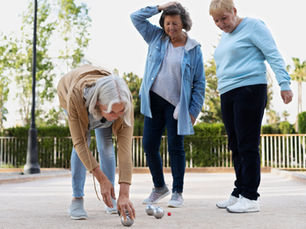 Drei ältere Damen spielen Boule draußen