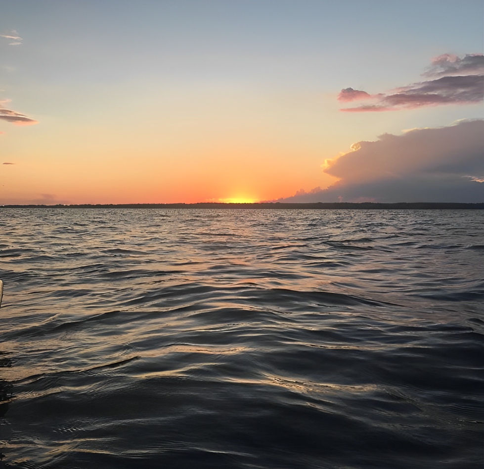 A breathtaking photograph capturing a vibrant sunset over the open ocean. The sky is adorned with warm hues of orange and yellow, creating a stunning display of colors. The sun, partially hidden behind a distant horizon, casts a golden glow on the calm and expansive water. The tranquil scene evokes a sense of serenity and awe-inspiring beauty.