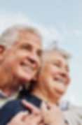 Photograph of an older couple, faces, smiling and looking out towards the right. Sky in the background.