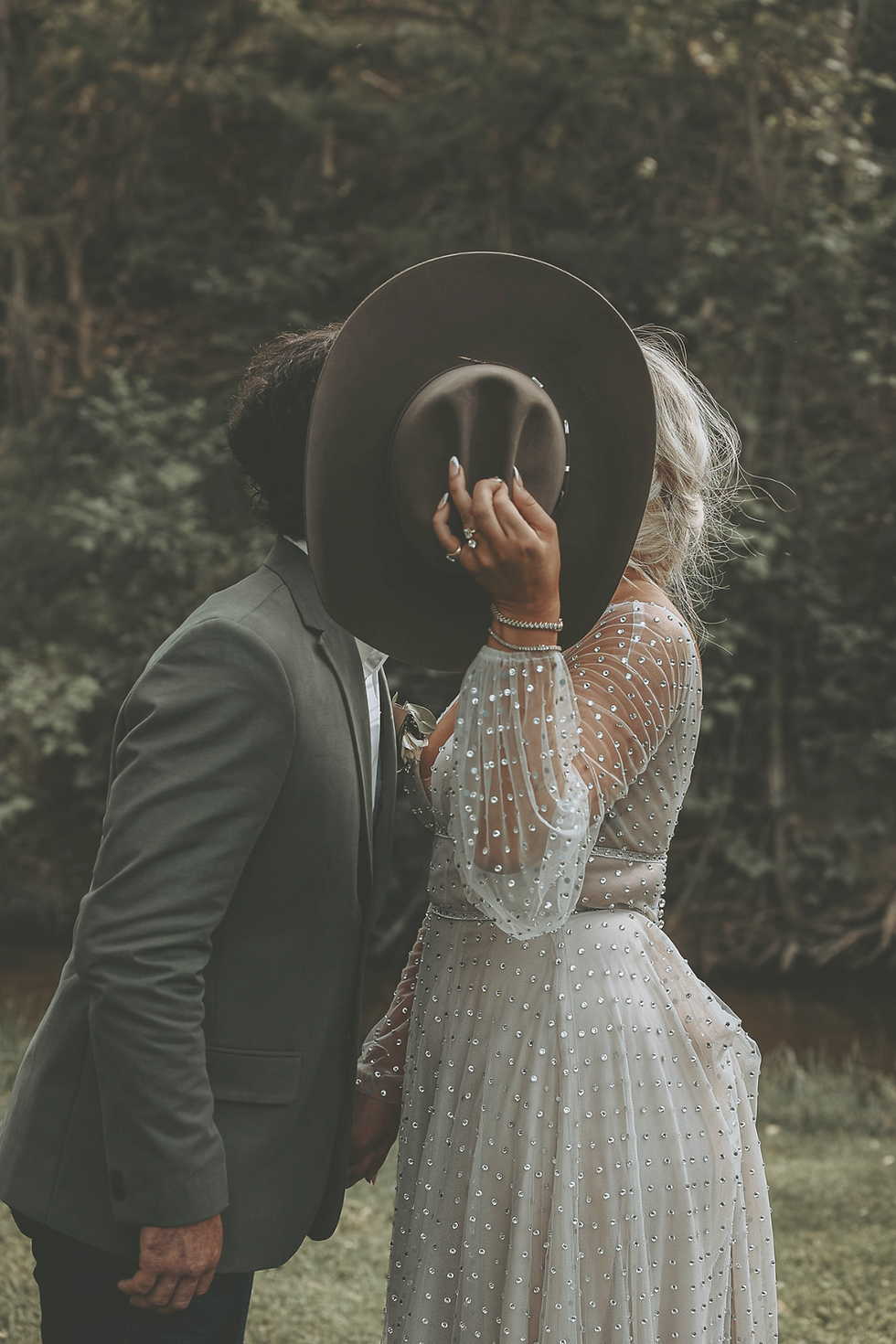 Romantic Western wedding moment – bride and groom share a kiss hidden behind a cowboy hat, with the