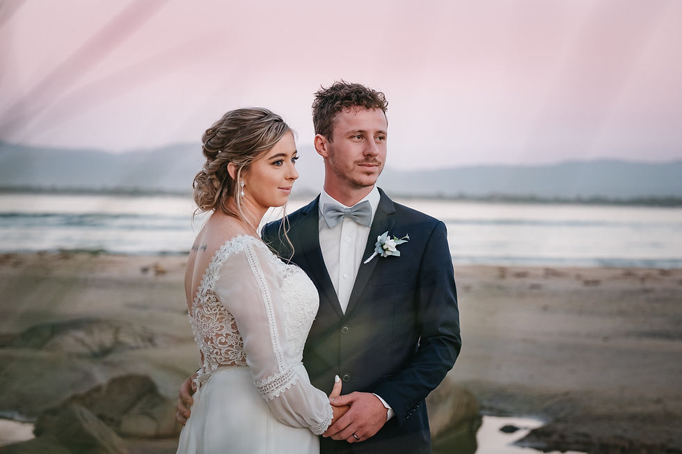 Newlyweds pose during sunset at the beach with scenic mountains background