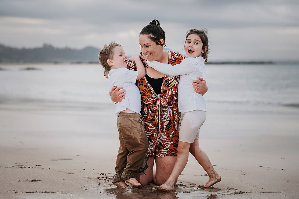 Woman hugging two children on beach; family enjoying outdoor time together.