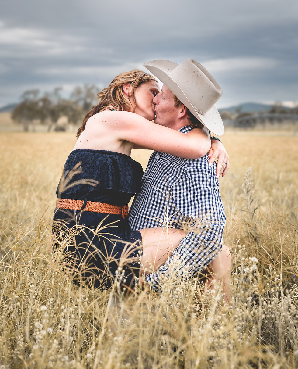 Couple kissing, man wearing a cowboy hat, embracing in tall grass field.