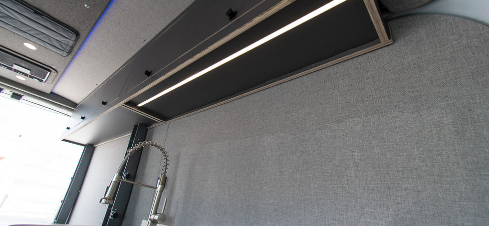Close-up view of the upper cabinets above the kitchen in a Transit camper van, featuring an LED light strip to enhance visibility for cooking and counter use in the Voyager layout.