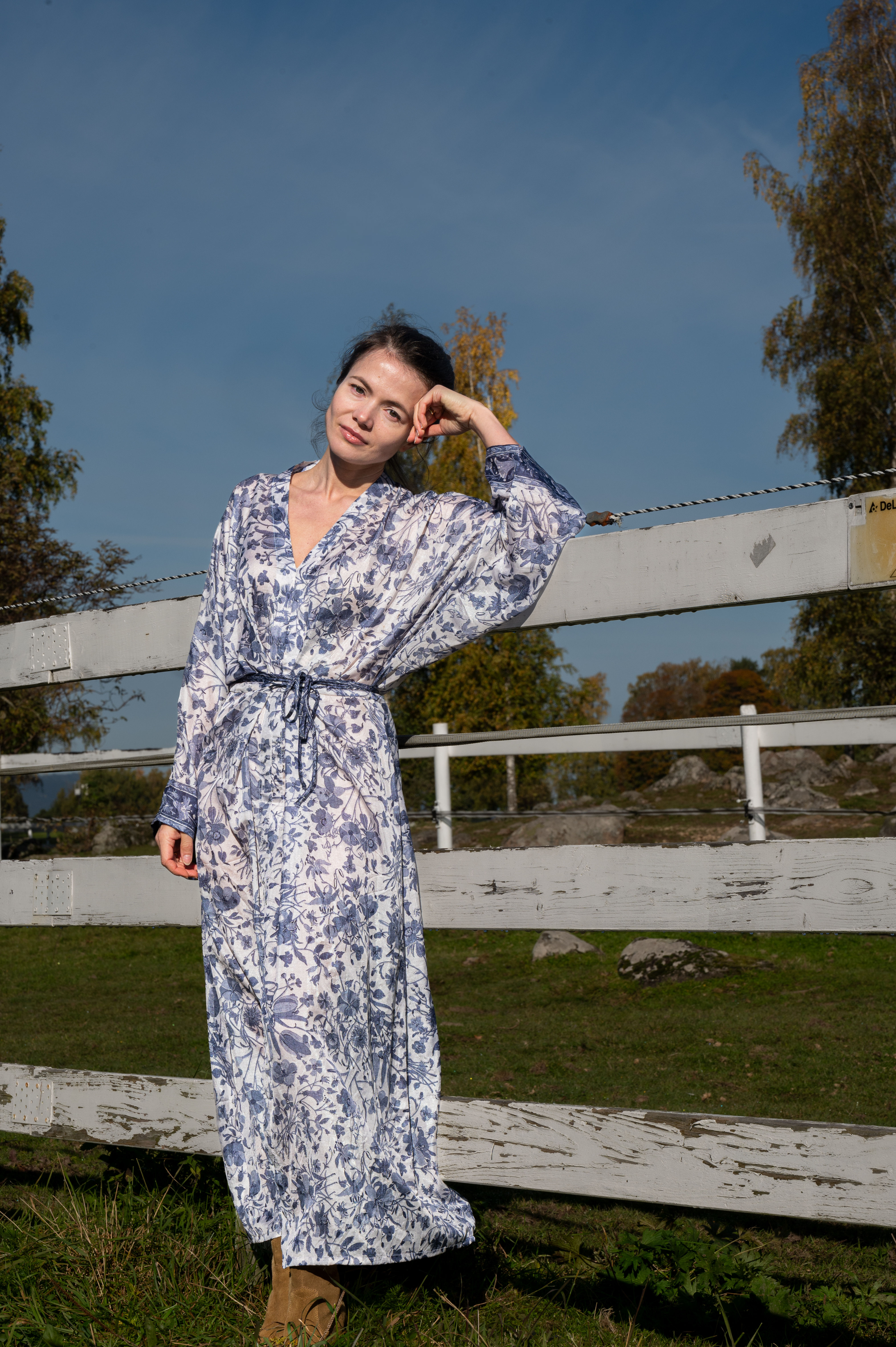girl is blue and white flower silk dress leaning against white fence outside