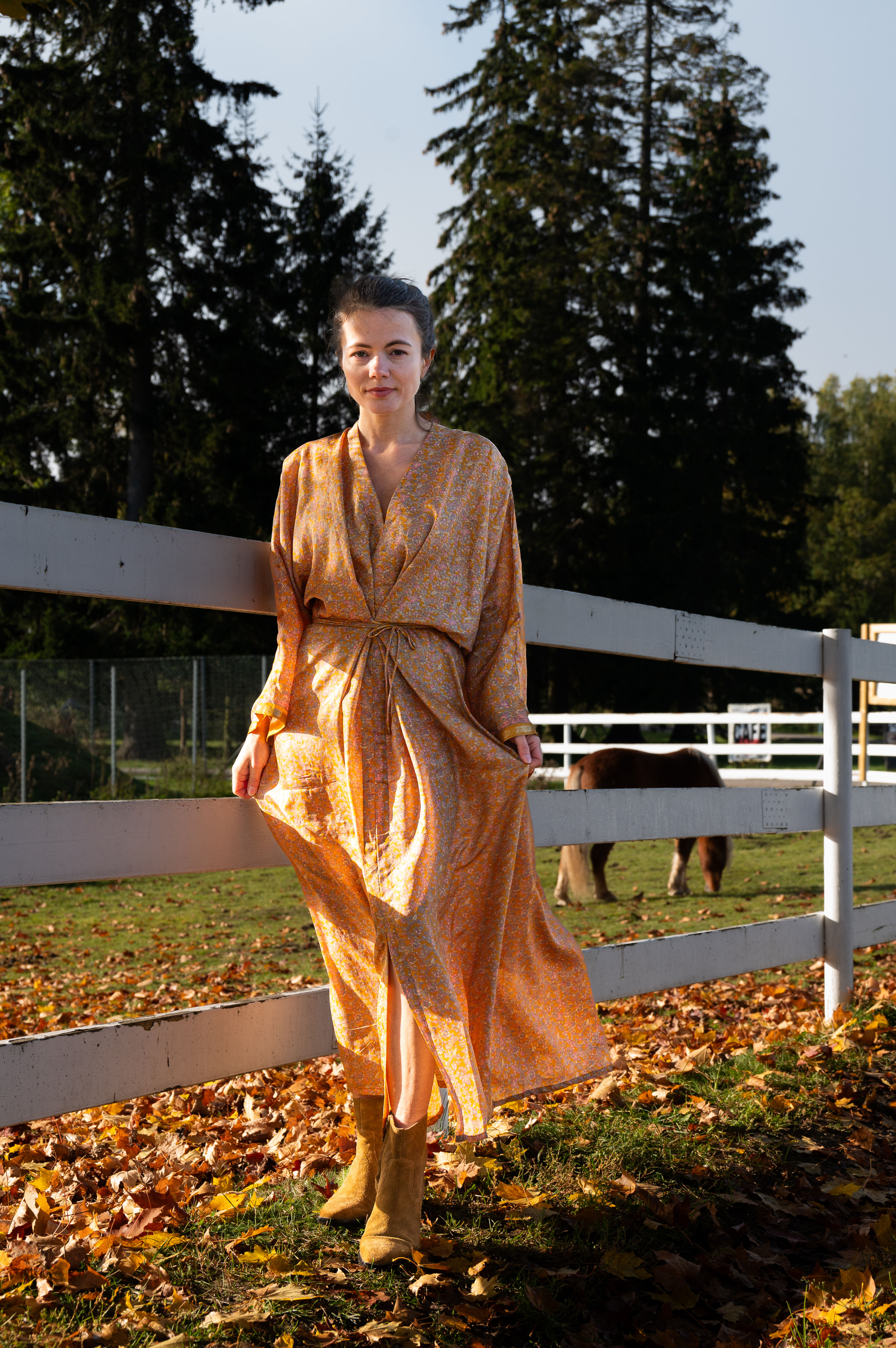 girl wearing autumn coloured silk dress with small flowers against white fence