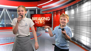 Two young children stand on a breaking news set holding mircophones and laughing
