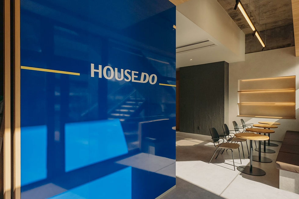 青い壁面に「HOUSEDO」と書かれた内装。シンプルなモダン・カフェスタイルの室内で、木製テーブルと椅子が並んでいる。明るい雰囲気。