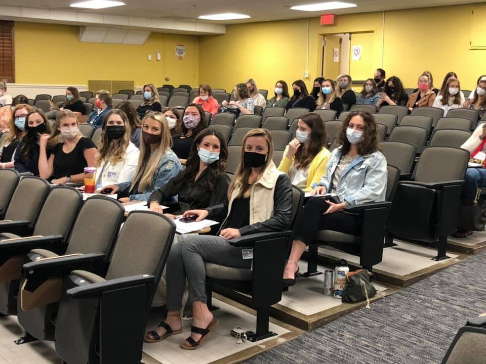 Audience members seated in an auditorium wearing masks.