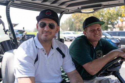 Two men smiling in golf cart at 7th Annual Golf Tournament