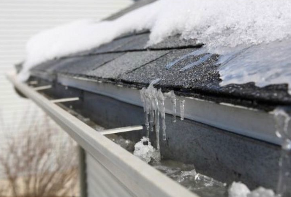 Close-up of an ice dam forming along the roof edge and gutters, showing icicles and melting snow that can cause leaks and shingle damage for homeowners in Mississauga, Etobicoke, Georgetown, Milton, and Oakville; used to illustrate the importance of professional ice dam removal and winter roof protection.