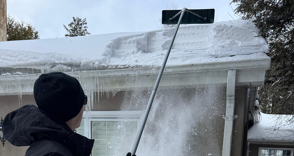 Worker removing snow and ice from a roof edge during winter conditions.