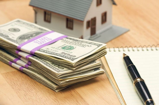 Stack of money beside a small house model and notebook illustrating budgeting and cost-saving strategies for roof replacements in Mississauga and the GTA.
