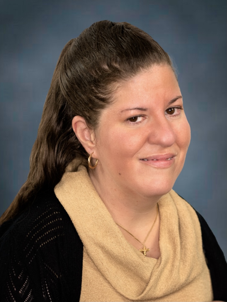 A headshot photo of a white woman with long brown hair. She is smiling at the viewer.
