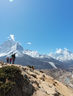 Hikers stand on rocky terrain with snow-capped mountains in the background under a clear blue sky, capturing a sense of adventure and vastness.