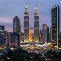 Kuala Lumpur skyline at dusk featuring the illuminated Petronas Twin Towers and surrounding skyscrapers, with a hazy purple sky.