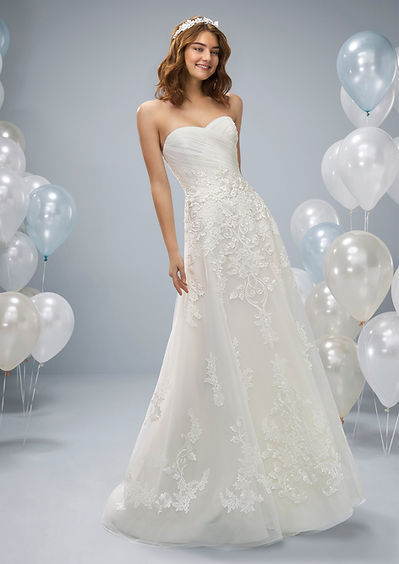 Woman in white wedding dress smiles, posing with balloons at home.