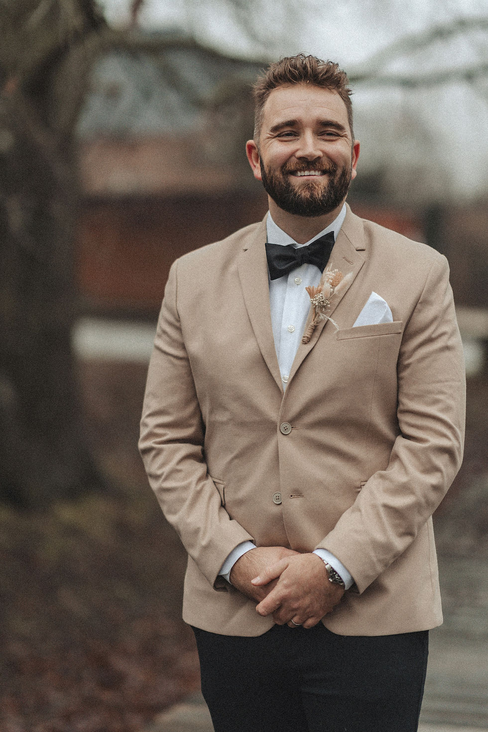 Smiling groom in a tan suit and bow tie, The Wedding Shop.