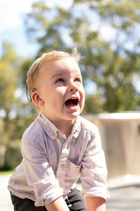 Photo of a young boy who is wearing a hearing aid looking happily up into the sky.